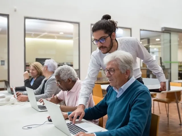 Oktató segít egy idősebb hallgatónak a laptopos gyakorlat közben